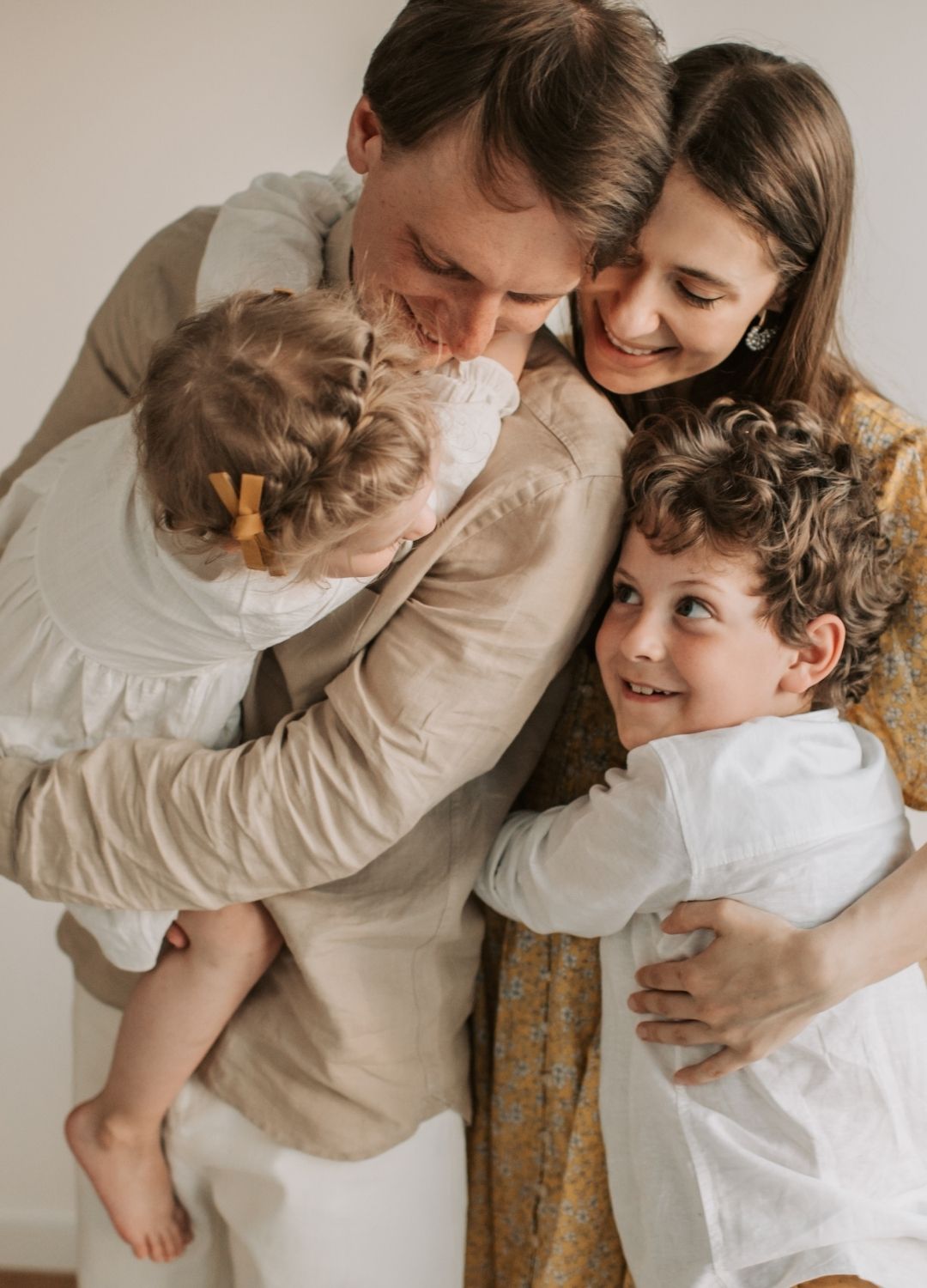 A man and woman hug two young children, a girl with braided hair and a bow, and a boy with curly hair.